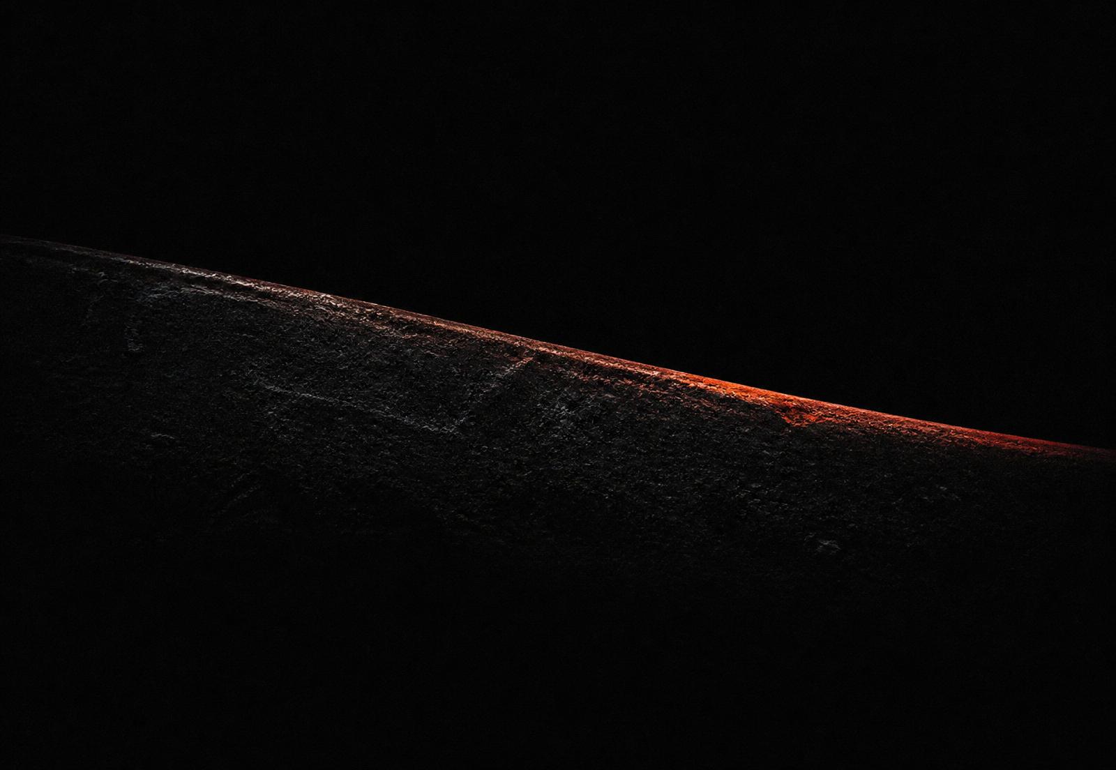 A single ember-lit edge of forged steel emerging from darkness